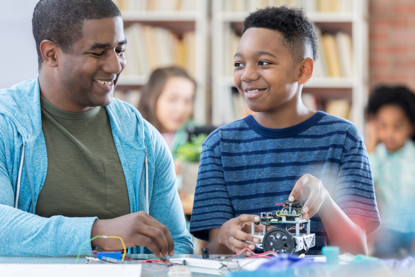 Male mentor and junior high student discussing robotics project and laughing